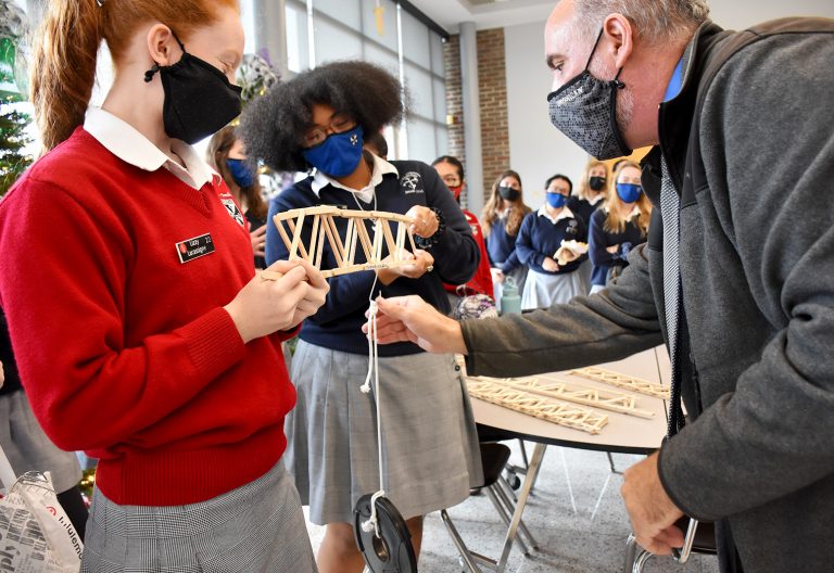 Students in Dominican's Engineering class test their popsicle bridges with weights.